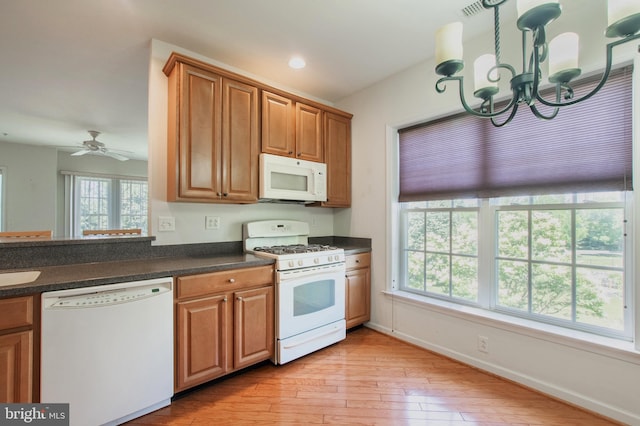 kitchen featuring light wood finished floors, dark countertops, hanging light fixtures, brown cabinetry, and white appliances