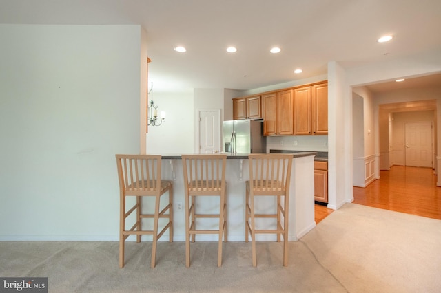 kitchen featuring light colored carpet, recessed lighting, stainless steel fridge, and a kitchen breakfast bar