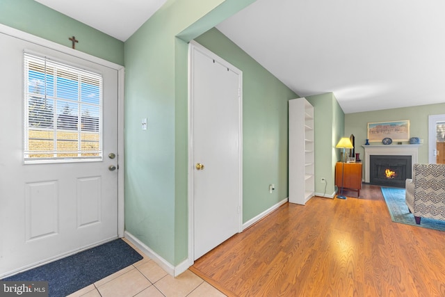 entryway with light wood-style floors, a lit fireplace, and baseboards