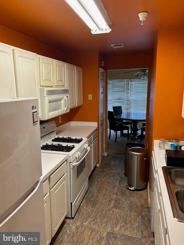 kitchen with visible vents, a sink, white cabinetry, white appliances, and light countertops