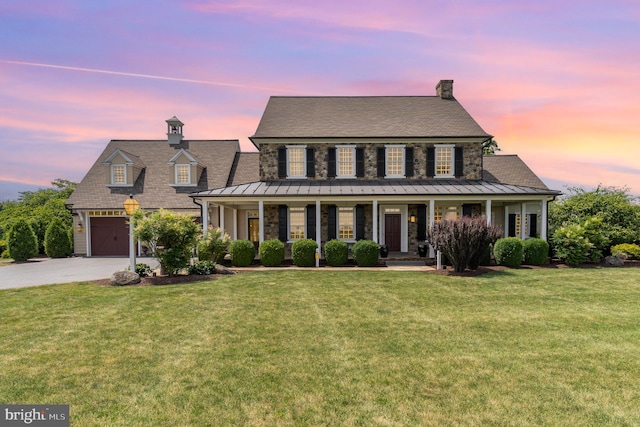 view of front of property featuring a porch, a standing seam roof, driveway, and a front lawn