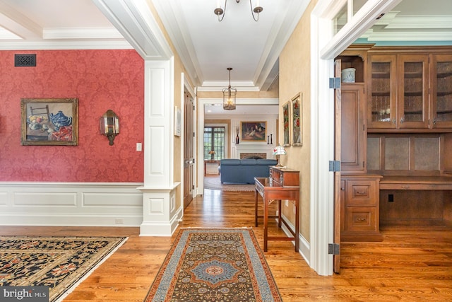 hall featuring wallpapered walls, visible vents, wainscoting, ornamental molding, and wood finished floors