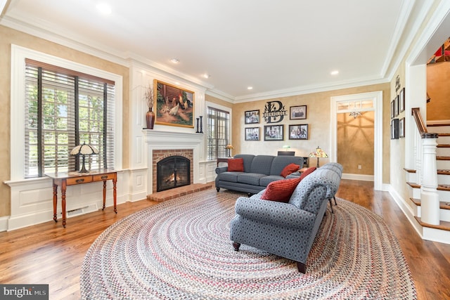 living area featuring stairway, wood finished floors, crown molding, a brick fireplace, and a decorative wall