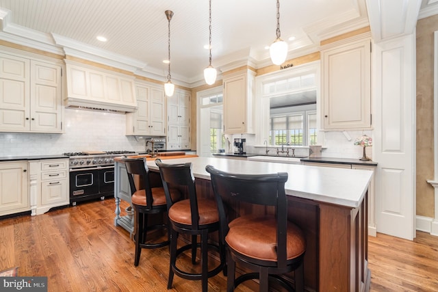 kitchen featuring range with two ovens, dark countertops, a kitchen island, cream cabinets, and pendant lighting