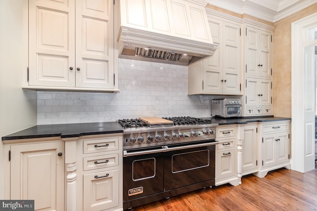 kitchen featuring dark countertops, custom exhaust hood, light wood-style floors, double oven range, and backsplash