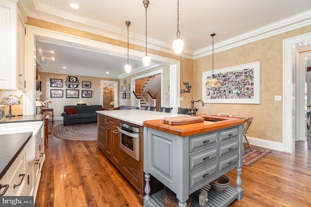 kitchen featuring hanging light fixtures, gray cabinetry, open floor plan, stainless steel oven, and an island with sink