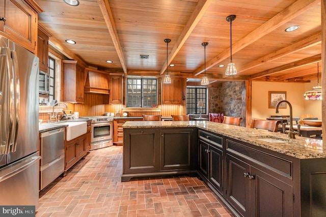 kitchen featuring brick floor, custom range hood, hanging light fixtures, appliances with stainless steel finishes, and a kitchen island