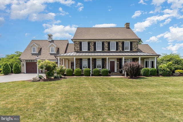 view of front of property featuring covered porch, driveway, a standing seam roof, and a front yard