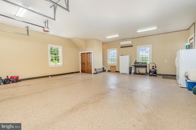 garage featuring baseboards, an AC wall unit, freestanding refrigerator, and a garage door opener