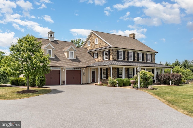 view of front of property with a front yard, a standing seam roof, covered porch, and driveway