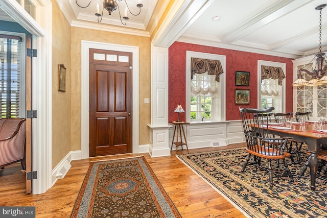 foyer entrance featuring a decorative wall, visible vents, ornamental molding, wood-type flooring, and an inviting chandelier