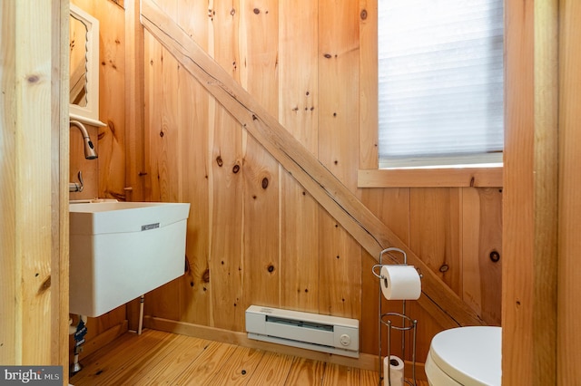 bathroom with toilet, a baseboard heating unit, a sink, wooden walls, and wood finished floors