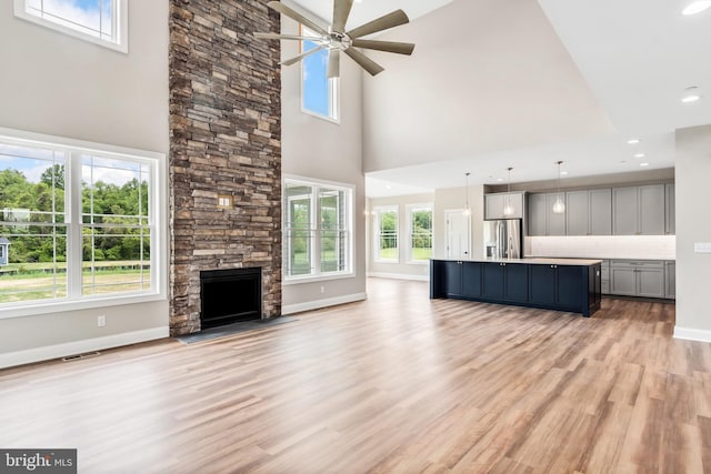 unfurnished living room featuring visible vents, baseboards, light wood-style flooring, ceiling fan, and a stone fireplace