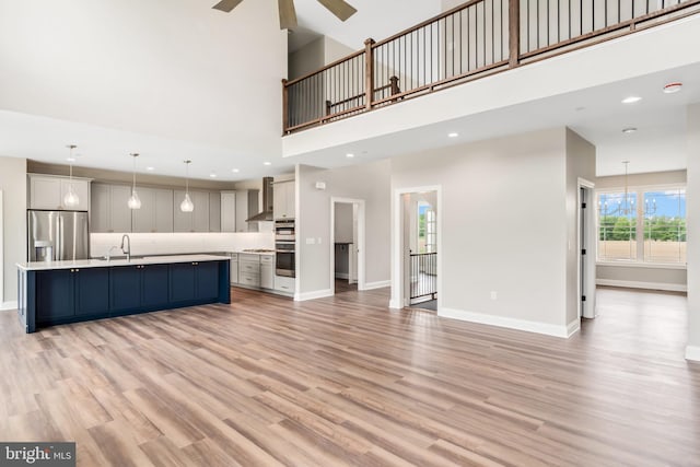 unfurnished living room with light wood-type flooring, a sink, a ceiling fan, and baseboards