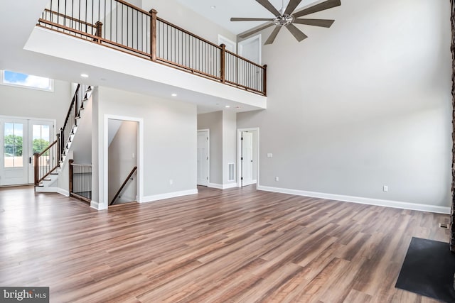 unfurnished living room featuring recessed lighting, a towering ceiling, wood finished floors, baseboards, and stairs