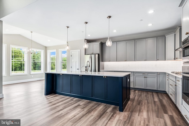 kitchen featuring gray cabinetry, light countertops, appliances with stainless steel finishes, hanging light fixtures, and a center island with sink