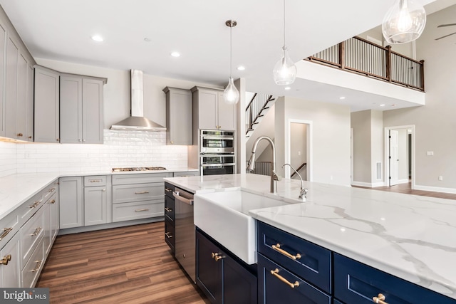 kitchen featuring a sink, appliances with stainless steel finishes, wall chimney exhaust hood, dark wood finished floors, and pendant lighting