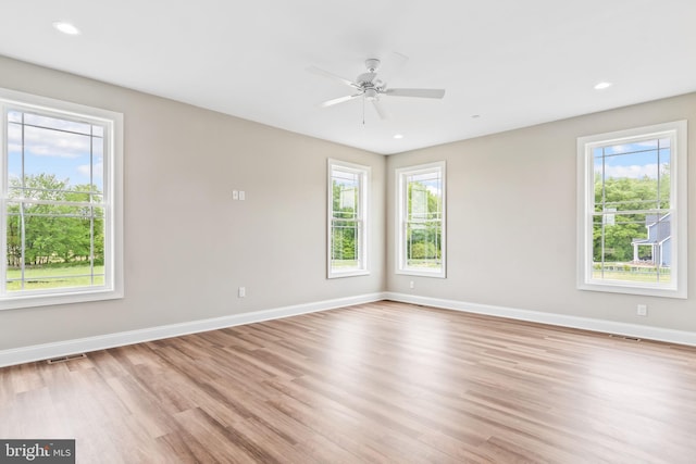 spare room with light wood-type flooring, a wealth of natural light, visible vents, and baseboards