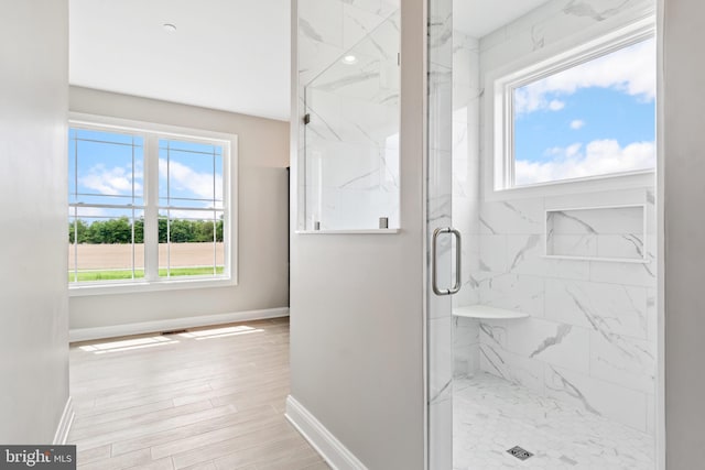 bathroom featuring a wealth of natural light, baseboards, a marble finish shower, and wood finished floors