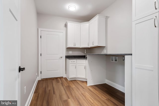 clothes washing area featuring hookup for a washing machine, cabinet space, light wood-style flooring, a sink, and baseboards