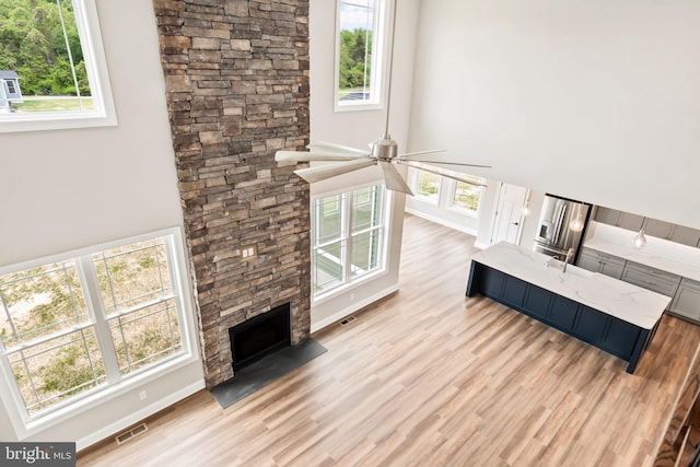 living room with light wood-style floors, visible vents, plenty of natural light, and a stone fireplace