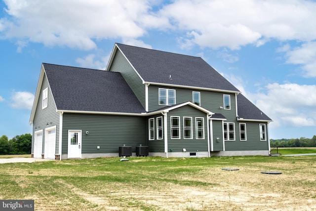 back of house featuring a garage, roof with shingles, and a lawn