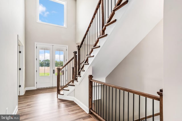 entryway featuring light wood finished floors, stairway, a towering ceiling, and baseboards