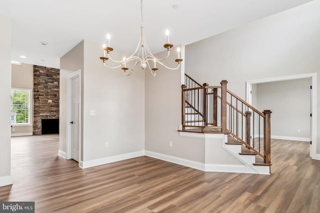 interior space with baseboards, a chandelier, wood finished floors, and a stone fireplace