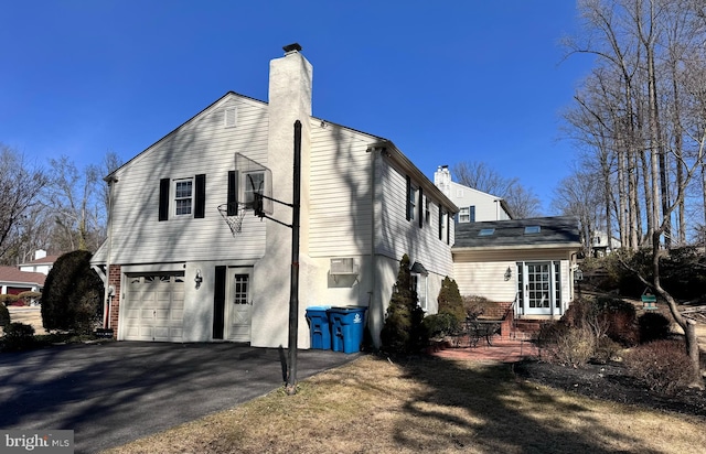 view of home's exterior featuring a garage, brick siding, a chimney, and aphalt driveway