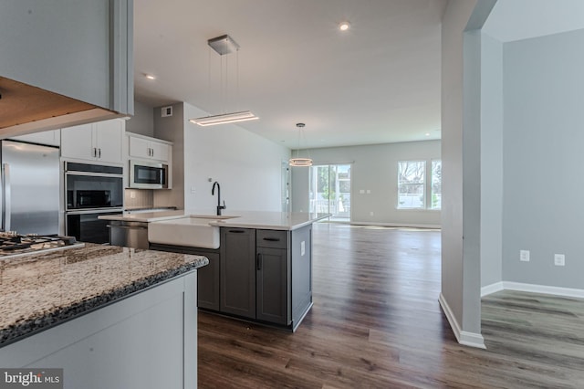 kitchen with a center island with sink, gray cabinets, hanging light fixtures, appliances with stainless steel finishes, and a sink