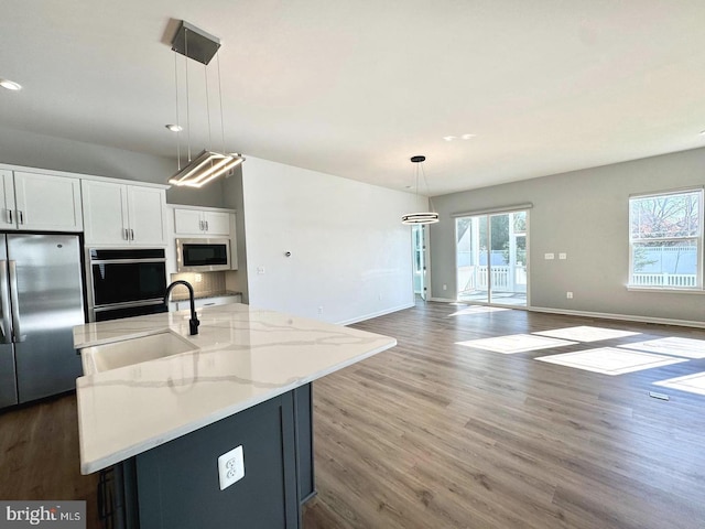 kitchen featuring pendant lighting, appliances with stainless steel finishes, open floor plan, a kitchen island with sink, and white cabinetry