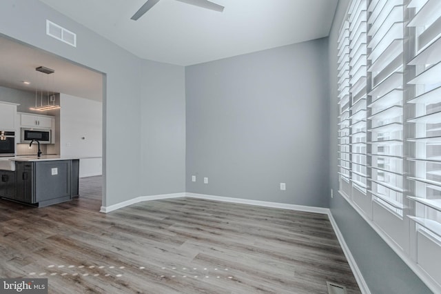 unfurnished room featuring a ceiling fan, visible vents, baseboards, and wood finished floors