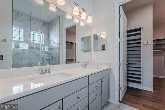 full bathroom featuring double vanity, a marble finish shower, baseboards, and a sink