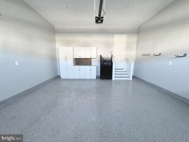 garage with baseboards, a garage door opener, and freestanding refrigerator