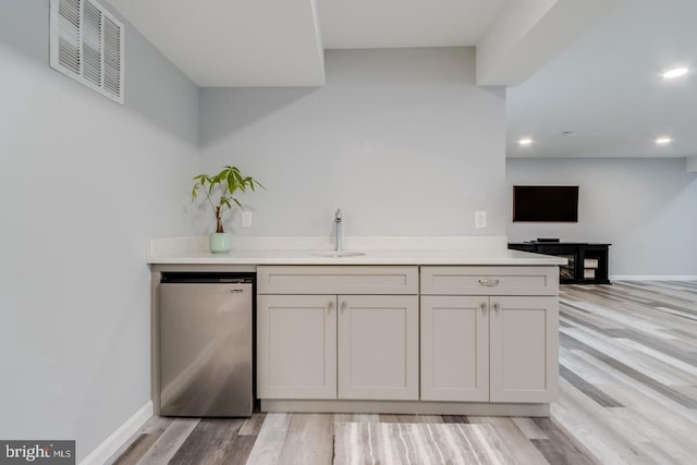 bar featuring baseboards, visible vents, light wood-style flooring, freestanding refrigerator, and a sink