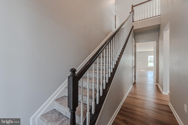 stairway featuring wood finished floors, a towering ceiling, and baseboards