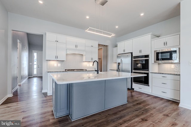 kitchen featuring stainless steel appliances, pendant lighting, white cabinetry, and a center island with sink