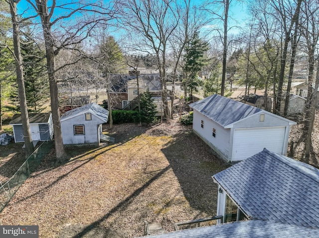 exterior space featuring roof with shingles, a detached garage, and an outbuilding