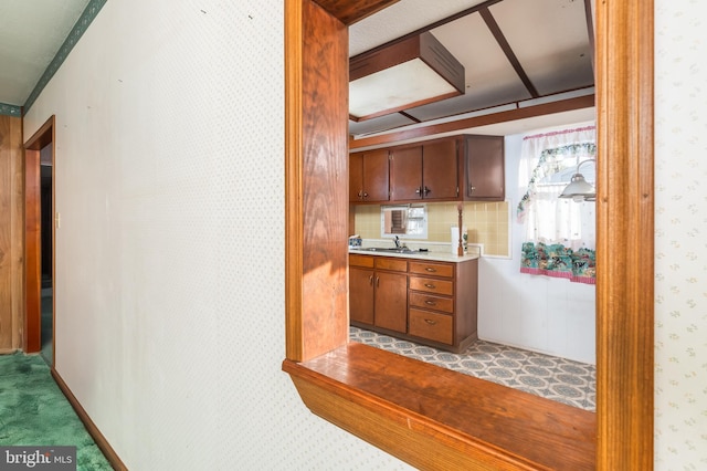 kitchen with light colored carpet, a sink, light countertops, brown cabinetry, and wallpapered walls