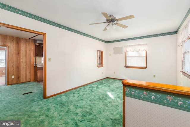 carpeted spare room featuring wood walls, baseboards, visible vents, and a ceiling fan