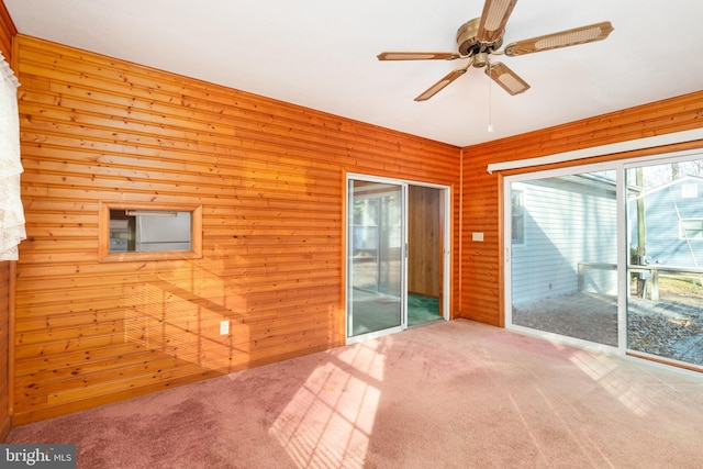 carpeted spare room with a ceiling fan and wooden walls