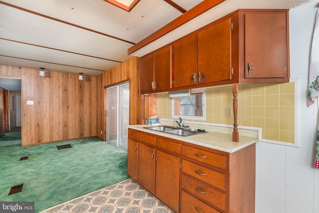 kitchen featuring light countertops, decorative backsplash, carpet flooring, a sink, and wood walls