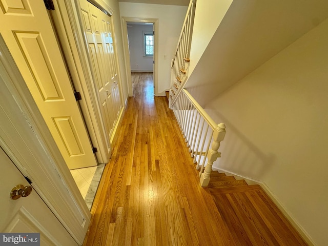 hallway with stairs, light wood finished floors, and baseboards