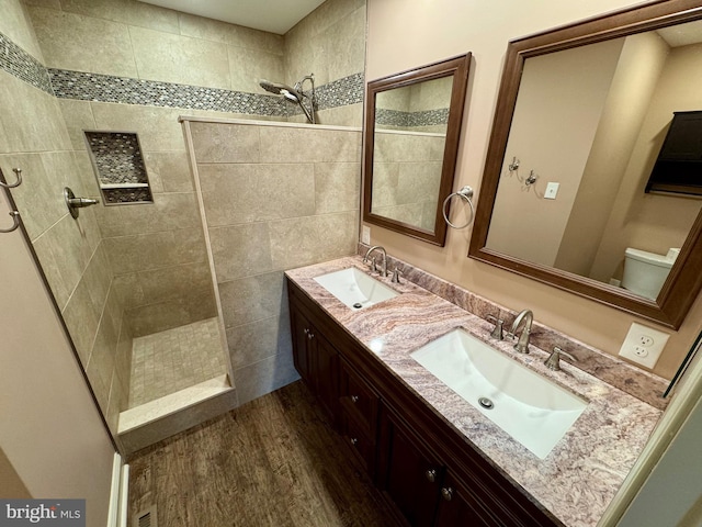 bathroom with a walk in shower, double vanity, wood finished floors, and a sink