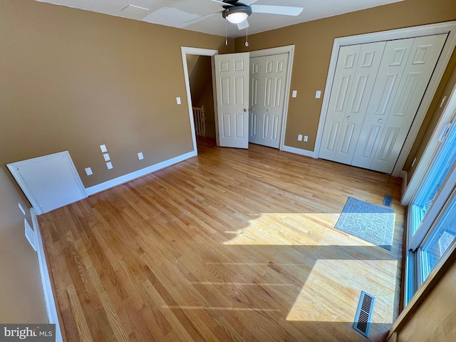 unfurnished bedroom featuring light wood-type flooring, a ceiling fan, baseboards, and multiple closets