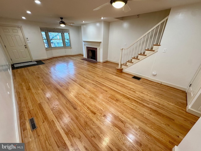 unfurnished living room featuring stairway, light wood-style flooring, a brick fireplace, and visible vents