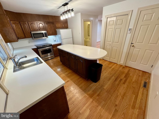 kitchen featuring pendant lighting, light countertops, appliances with stainless steel finishes, a sink, and light wood-type flooring