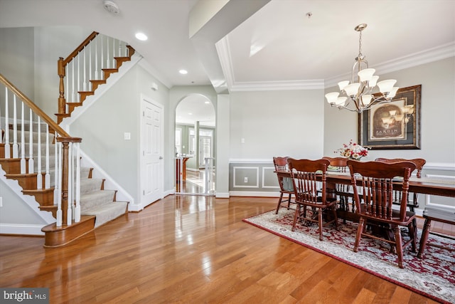 dining room with arched walkways, a notable chandelier, stairway, ornamental molding, and wood finished floors