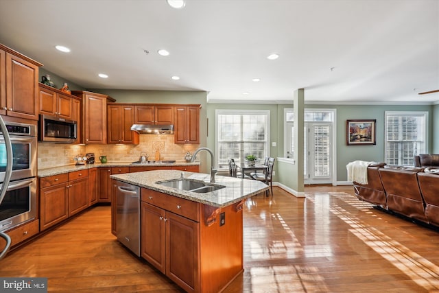 kitchen featuring decorative backsplash, open floor plan, stainless steel appliances, under cabinet range hood, and a sink