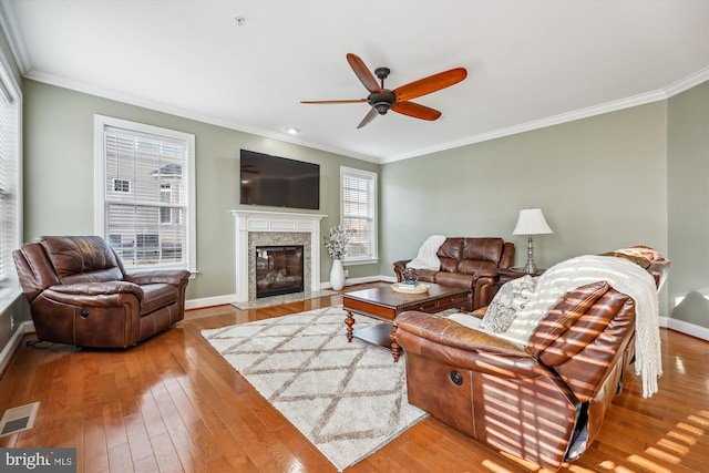 living room with crown molding, a fireplace, visible vents, baseboards, and hardwood / wood-style flooring